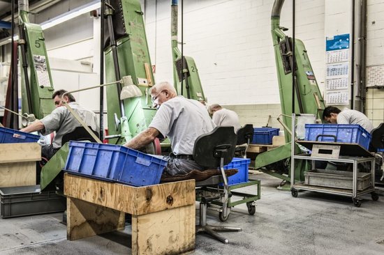 Mannen aan het werk in een fabriek met grote groene machines en blauwe kratten.