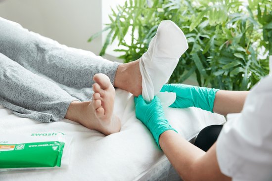 Voeten worden behandeld met witte Swash Foot Caps, omringd door groen met een pakje Swash Foot Cap op de achtergrond.