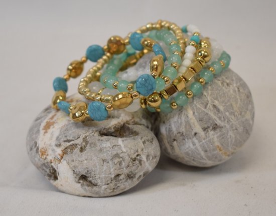 Een stapel van zeven elastische armbanden met witte, turquoise en gouden kralen, in Ibiza/Boho-stijl.