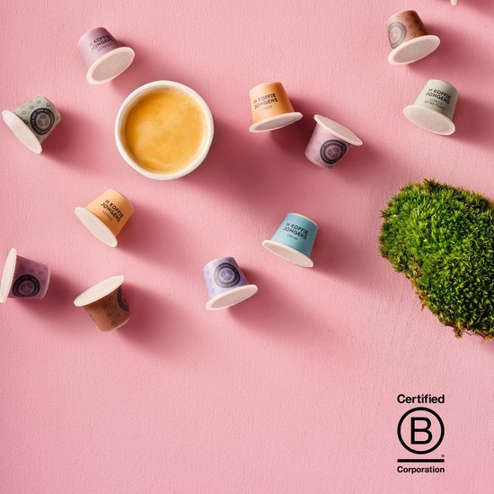 Veelkleurige composteerbare koffiecups op een roze achtergrond, met een kopje koffie en een stukje mos.