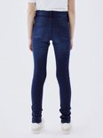 Achterkant van een meisje in een donkerblauwe skinny jeans en witte sneakers.