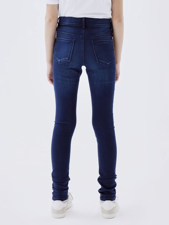 Achterkant van een meisje in een donkerblauwe skinny jeans en witte sneakers.