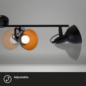 Detailopname van een zwarte plafondspot met gouden binnenkant. De lamp is verstelbaar.