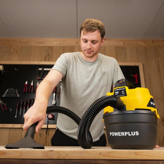 Een man gebruikt een gele en zwarte Powerplus nat-droog stofzuiger om een werkbank schoon te maken.