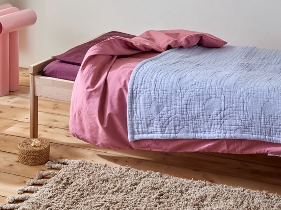 Een lavendelblauwe mousseline spreideken over een kinderbed met roze beddengoed.