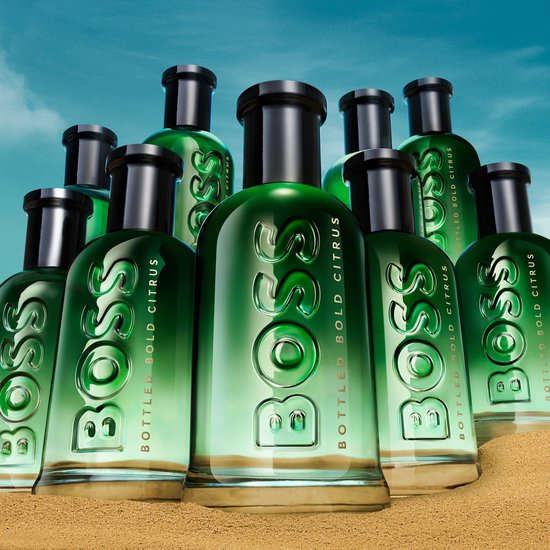 Een collectie BOSS BOTTLED BOLD CITRUS Eau de Parfum flessen op een zandige ondergrond.