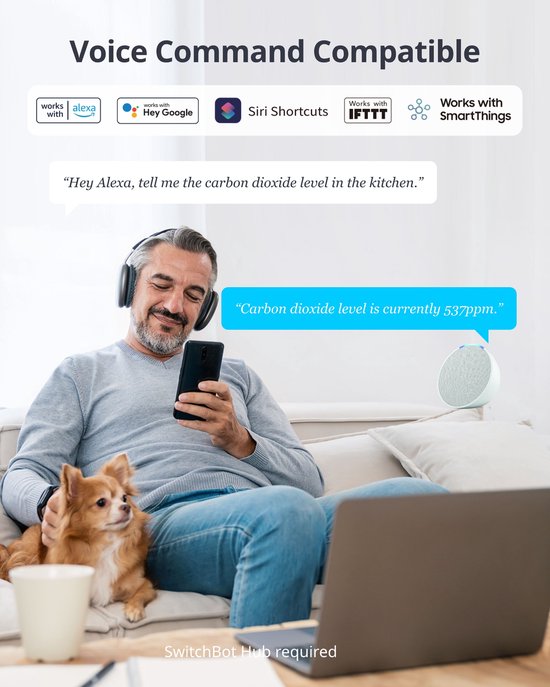 Man zit op bank met telefoon, draadloze koptelefoon op en hondje op schoot. Tekst: 'Voice Command Compatible'.