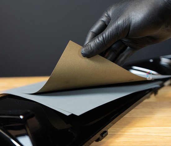 Een hand met zwarte handschoen houdt een grijs schuurvel vast boven een glanzend zwart oppervlak.