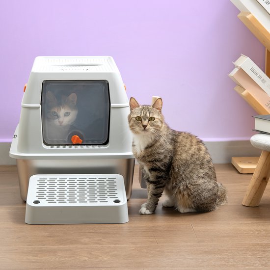Grijze top entry kattenbak met een grijze tabby kat ervoor. Een tweede kat kijkt uit het raam van de bak. In een woonkamer setting.