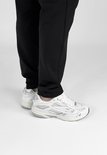 Persoon draagt witte "DUTCH'D" sneakers met zilveren accenten en zwarte broek.