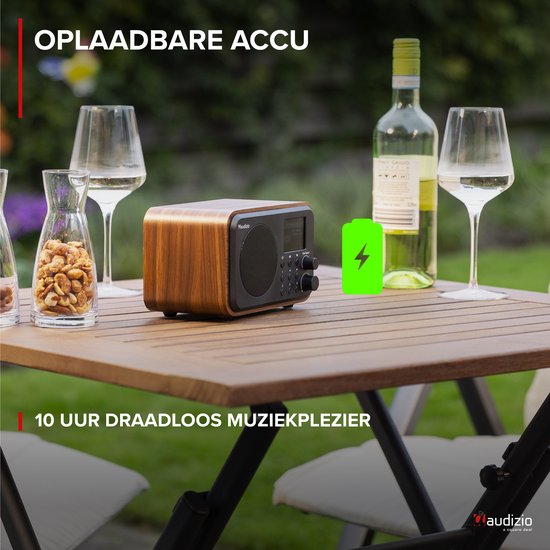 DAB radio met houten behuizing op een tuintafel, naast wijnglazen en een fles wijn. Batterijsymbool met bliksemschicht.