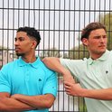 Twee mannen buiten bij een hek, één in turquoise polo, de ander in lichtgroene polo.