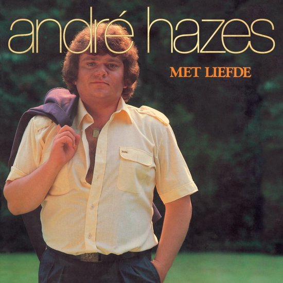 André Hazes met paarse jas over zijn schouder, gele blouse met opstaande kraag, donkerblauwe broek.