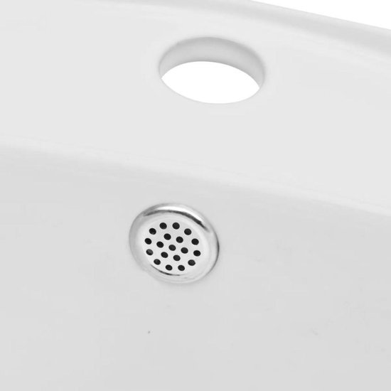Détail d'un bouchon de vidange chromé perforé dans un lavabo blanc.