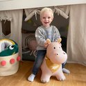 Kind op een lichtroze skippend Nijlpaard met gele bandana, in slaapkamer.