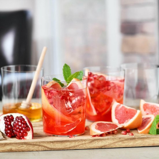 Drie glazen gevuld met rode drank, grapefruit, granaatappel en munt, op een houten plank.