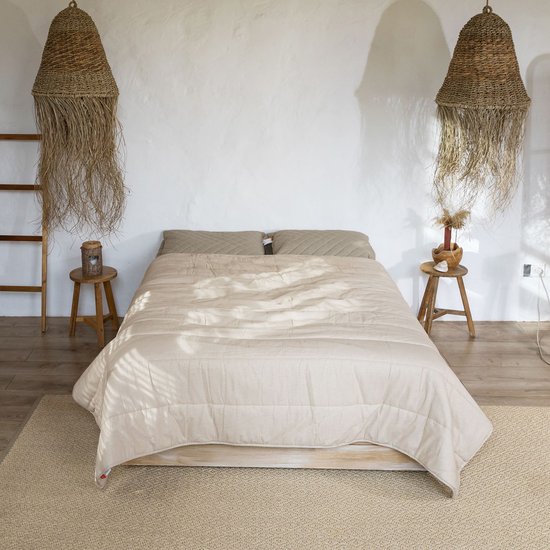 Wit slaapkamerinterieur met een tweepersoonsbed opgemaakt met een beige hennep dekbed.