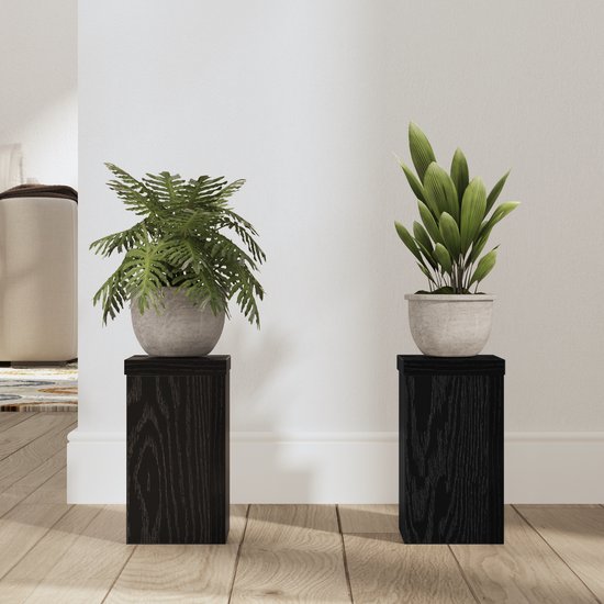 Twee zwarte houten plantenstandaards met een eikennerfstructuur, elk met een plant in een grijze pot.