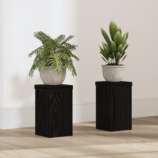 Twee zwarte houten plantenstandaards met een eikennerfstructuur, elk met een plant in een grijze pot erop.