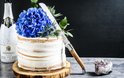 Gebakken taart met blauwe hortensia's en een Laguiole mes, naast een fles champagne.