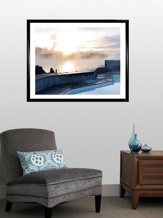 Un décor de salon moderne avec un grand cadre photo noir sur le mur, au-dessus d'un fauteuil gris.