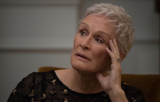Close-up van een vrouw met kort, grijs haar, die met haar hand tegen haar slaap leunt, ze draagt een zwart versierd jurkje.