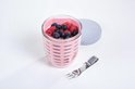 Gobelet à fruits rose avec framboises et myrtilles, extérieur perforé et une fourchette à côté.