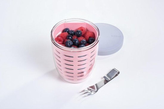 Gobelet à fruits rose avec framboises et myrtilles, extérieur perforé et une fourchette à côté.