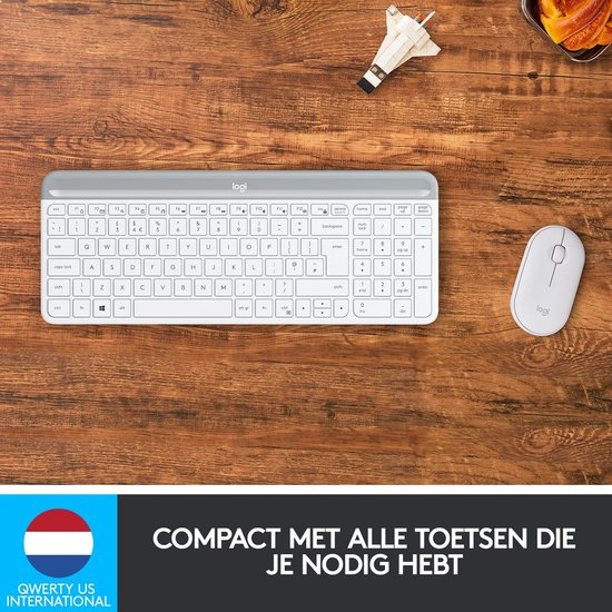 Wit Logitech toetsenbord en muis op houten bureau, met speelgoed.
