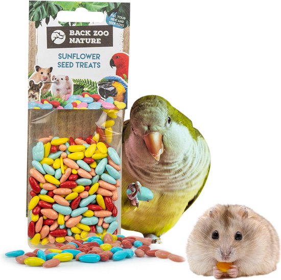 Een zakje met veelkleurige, ovale vogelsnoepjes, geel, rood, lichtblauw en roze, ligt naast een parkiet en een hamster die een traktatie eet.