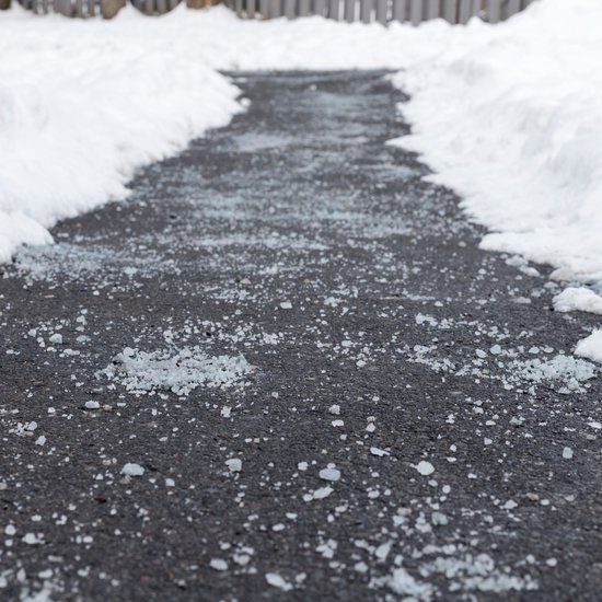 Een weg bedekt met strooizout tussen besneeuwde bermen.