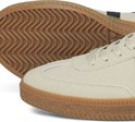 Close-up van de crèmekleurige sneaker met profielzool en bruine rand.