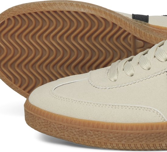 Close-up van de crèmekleurige sneaker met profielzool en bruine rand.
