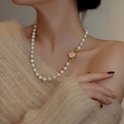 Crèmekleurige parelketting met een gouden bloemvormige sluiting, gedragen door een vrouw met een beige trui.