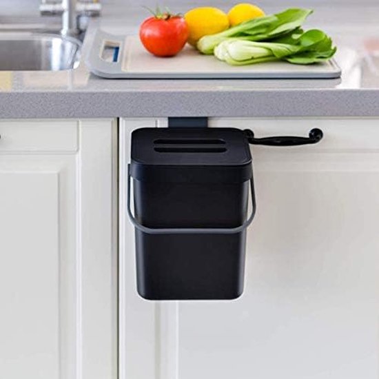 Zwarte compostbak hangt aan een keukenkastje, naast een snijplank met groenten en fruit.