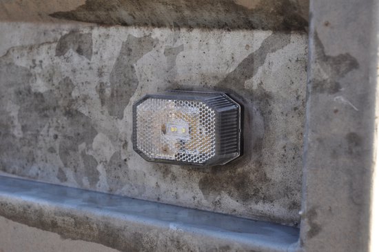 Achterlicht met twee witte LED's, geribbeld, transparant kunststof, gemonteerd op een betonnen muur.
