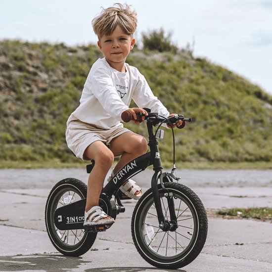 Petit garçon aux cheveux blonds sur un vélo Deryan noir 3-en-1 avec guidon et selle marrons. Il porte un t-shirt blanc et un short beige.