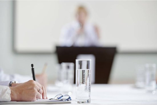 Hand schrijft met een zwarte pen naast een bril en een glas water.