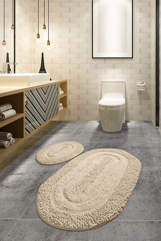 Badkamer met twee beige ovale badmatten op grijze tegels, bij een wastafel en toilet.