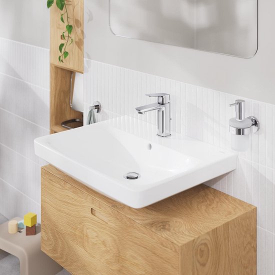 Moderne badkamer met houten meubel, witte wasbak en chromen zeepdispenser.