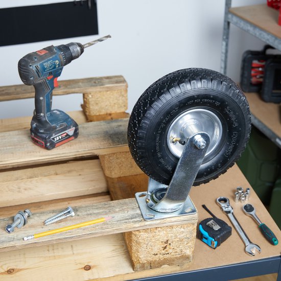 Zwart luchtband zwenkwiel gemonteerd op een houten pallet, met een boormachine en gereedschap op de achtergrond.