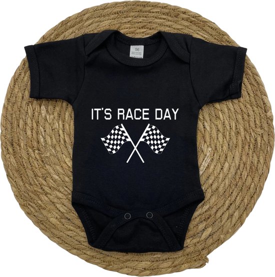 Zwart babyrompertje met 'IT'S RACE DAY' en finishvlaggen, gepresenteerd op een ronde rieten mat.