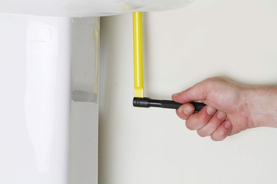 Man gebruikt een gele kraanmoersleutel op een witte wasbak.