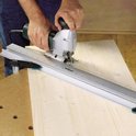 Een persoon gebruikt een wolfcraft decoupeerzaag met een geleiderail om een rechte snede te maken in een houten plank.