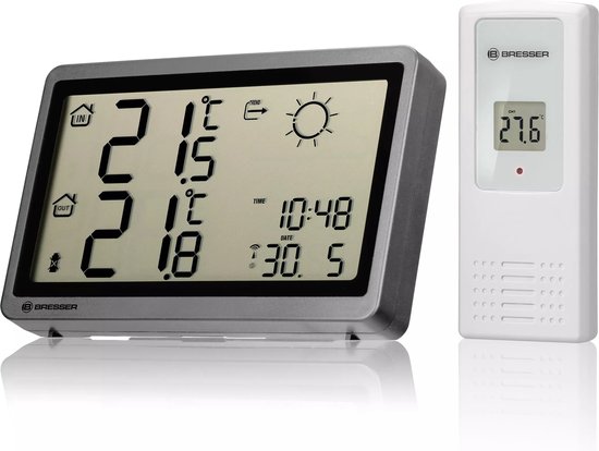 Een antracietkleurig weerstation met een digitale display die de binnen- en buitentemperatuur weergeeft. Een losse witte sensor staat ernaast.