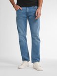 Man in zwart shirt en lichtblauwe jeans, staand met hand in zak.