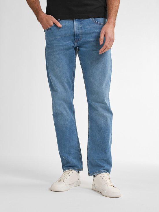 Man in zwart shirt en lichtblauwe jeans, staand met hand in zak.