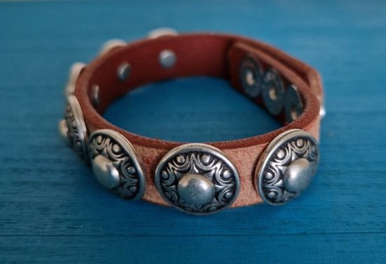 Bruine leren armband met zilverkleurige studs, op blauwe houten achtergrond.