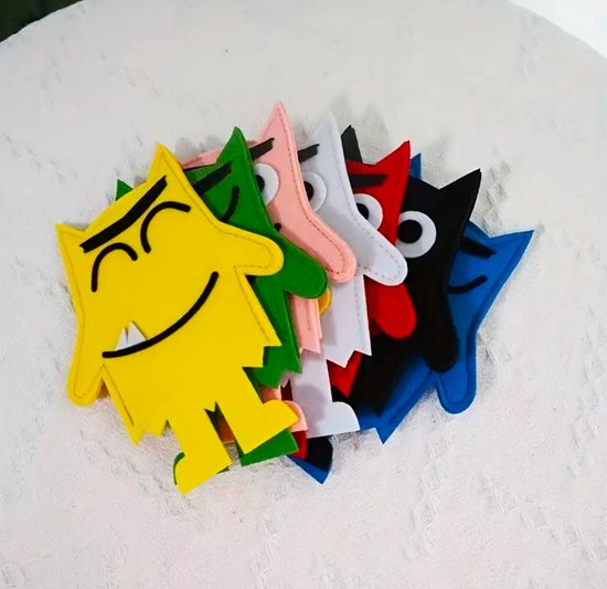 Een rij van zes vilten vingerpoppen in verschillende kleuren: geel, groen, roze, wit, rood en zwart. Elke pop heeft een monstergezicht met ogen, mond en hoektanden.