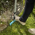 Persoon met bruine schoenen gebruikt de turquoise graskantafsteker op gras bij een stenen rand.